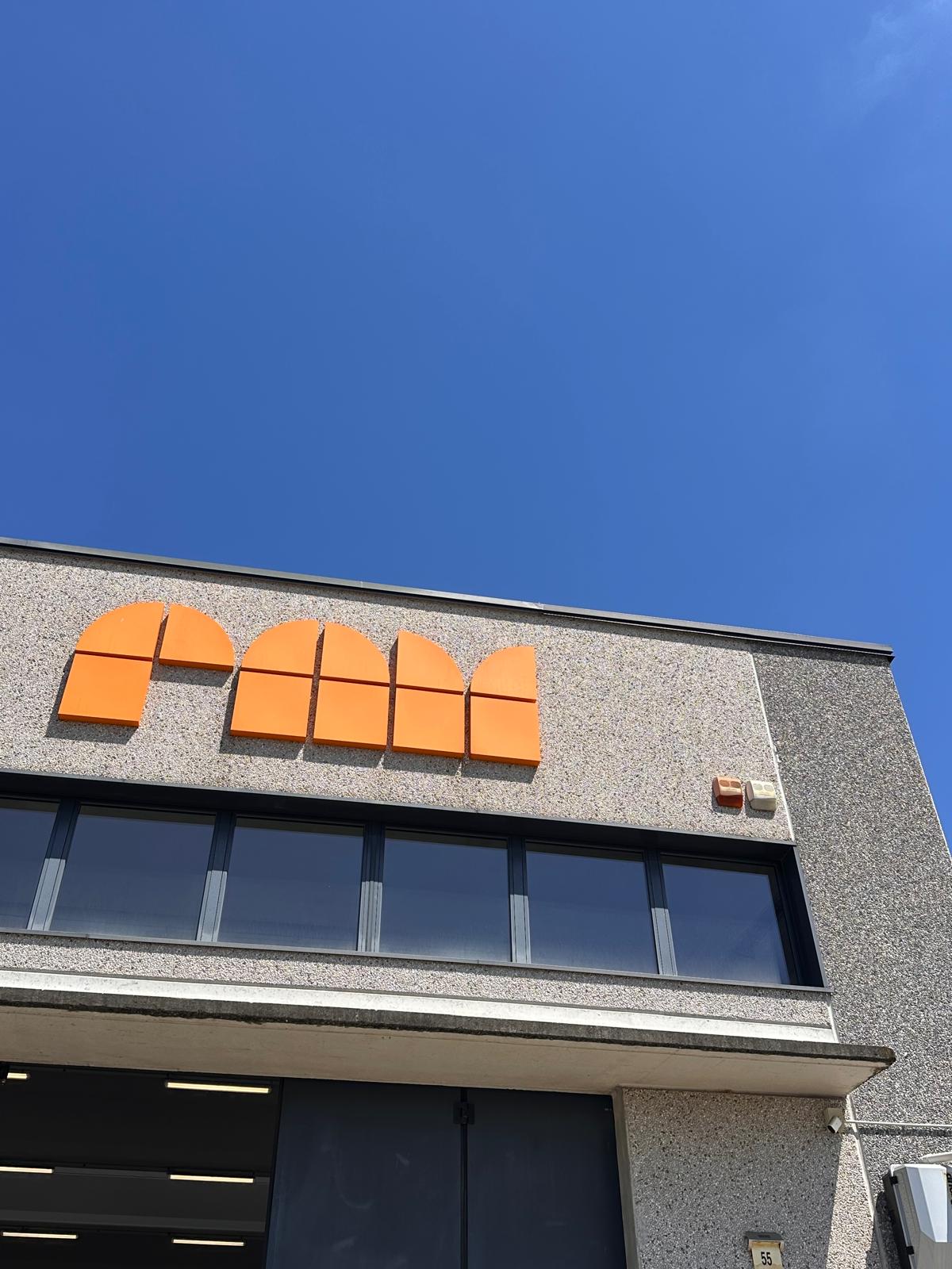 Facciata di edificio industriale con insegna arancione e cielo azzurro limpido sopra.