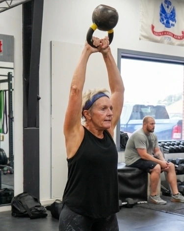 Woman performs an overhead kettlebell exercise during a group fitness class.