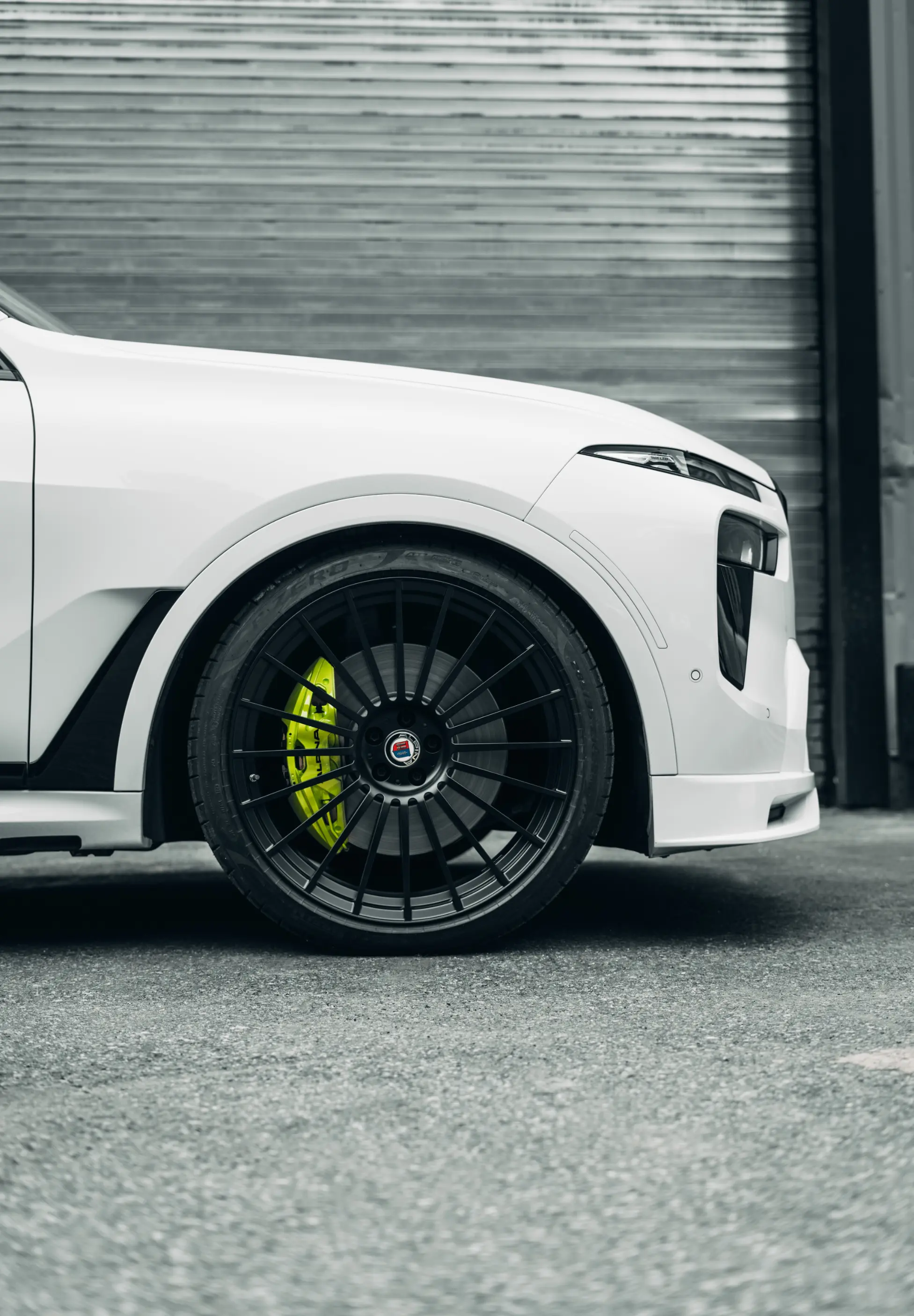 White BMW X7 with a lime green painted brake caliper behind a black Alpina-style wheel