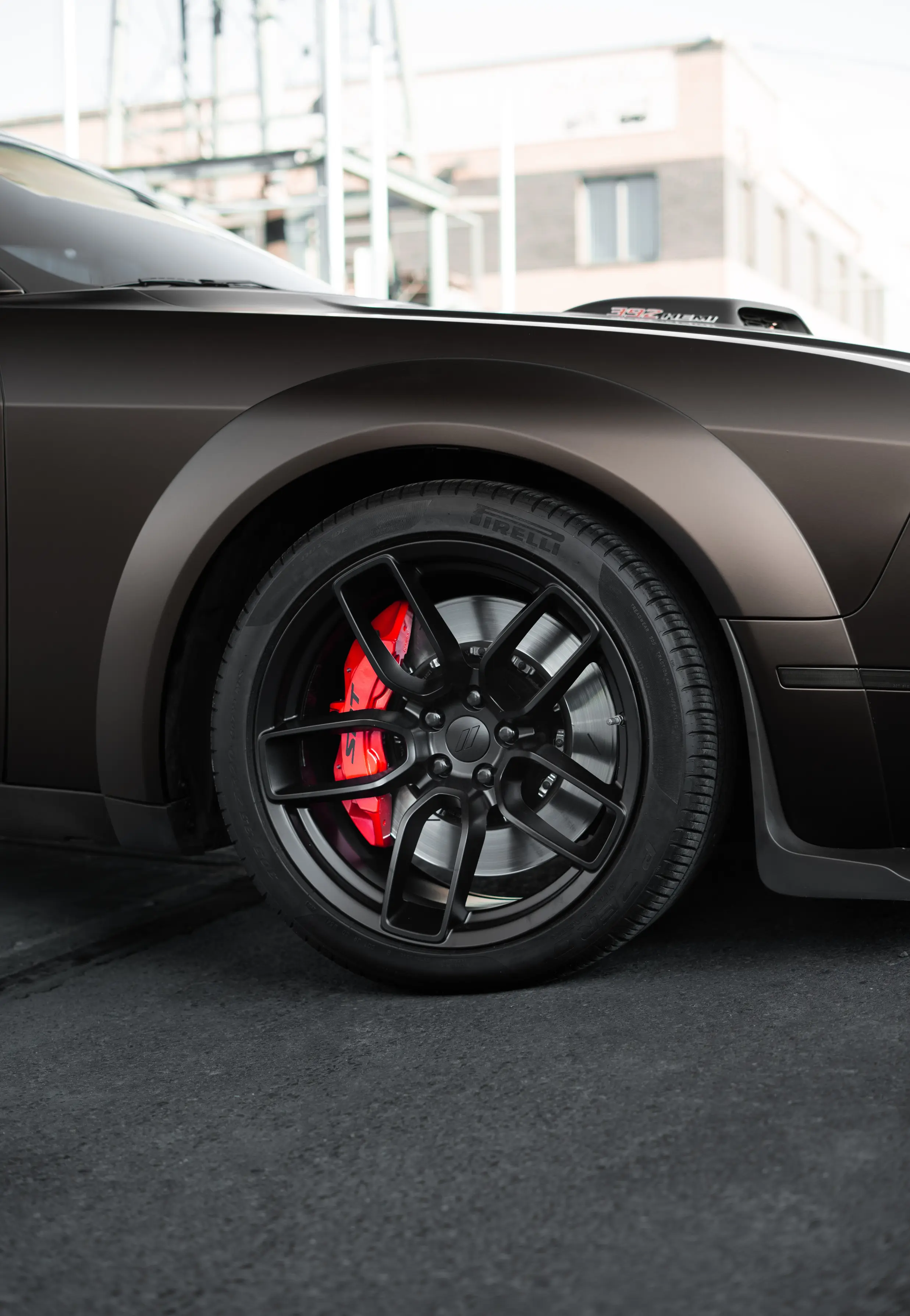 Red painted brake caliper on a matte brown Dodge Challenger