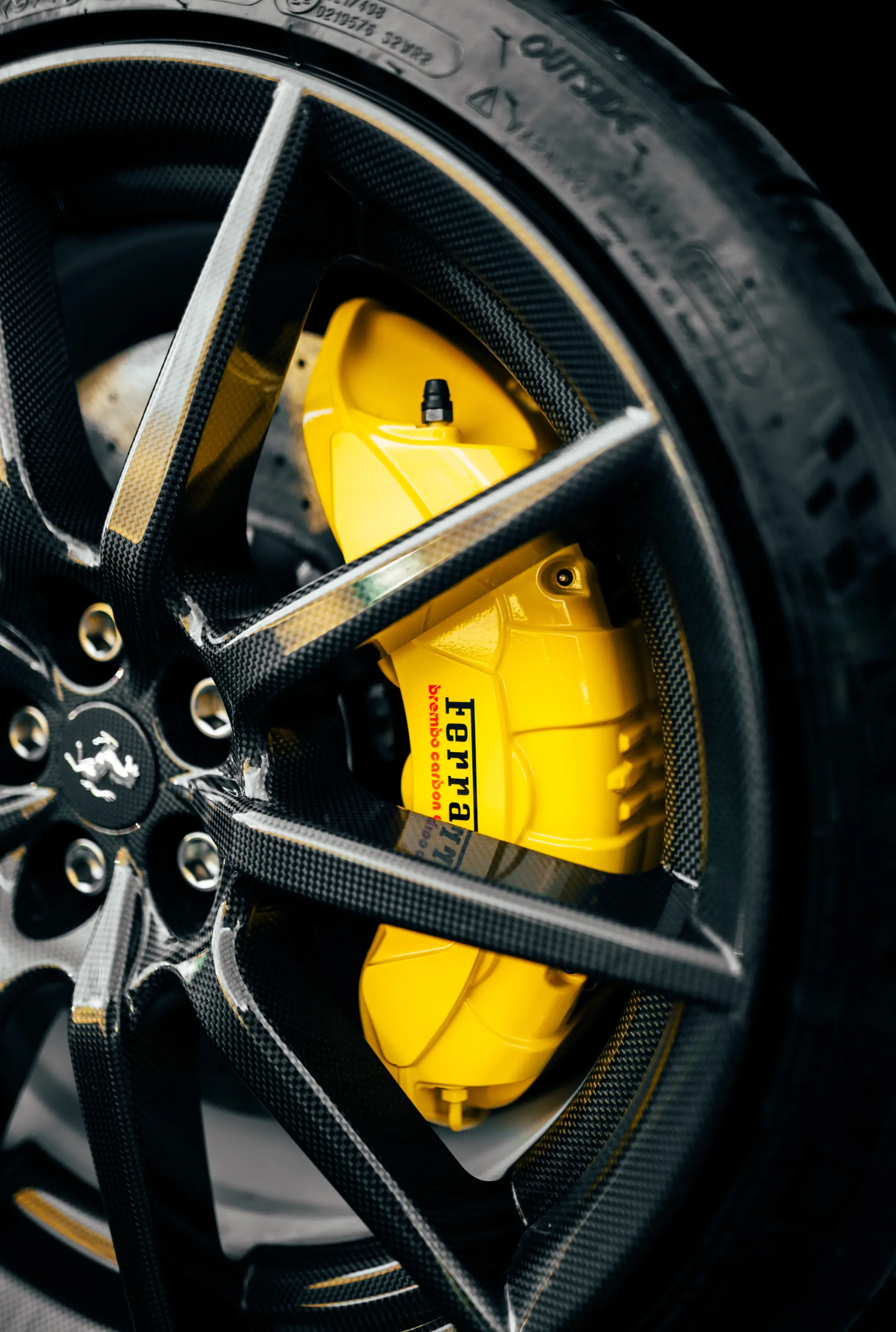 Yellow painted Ferrari Brembo brake caliper behind a carbon fiber wheel