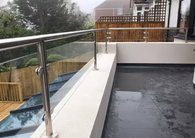 A modern balcony with glass and metal railing overlooks a garden on a foggy day.
