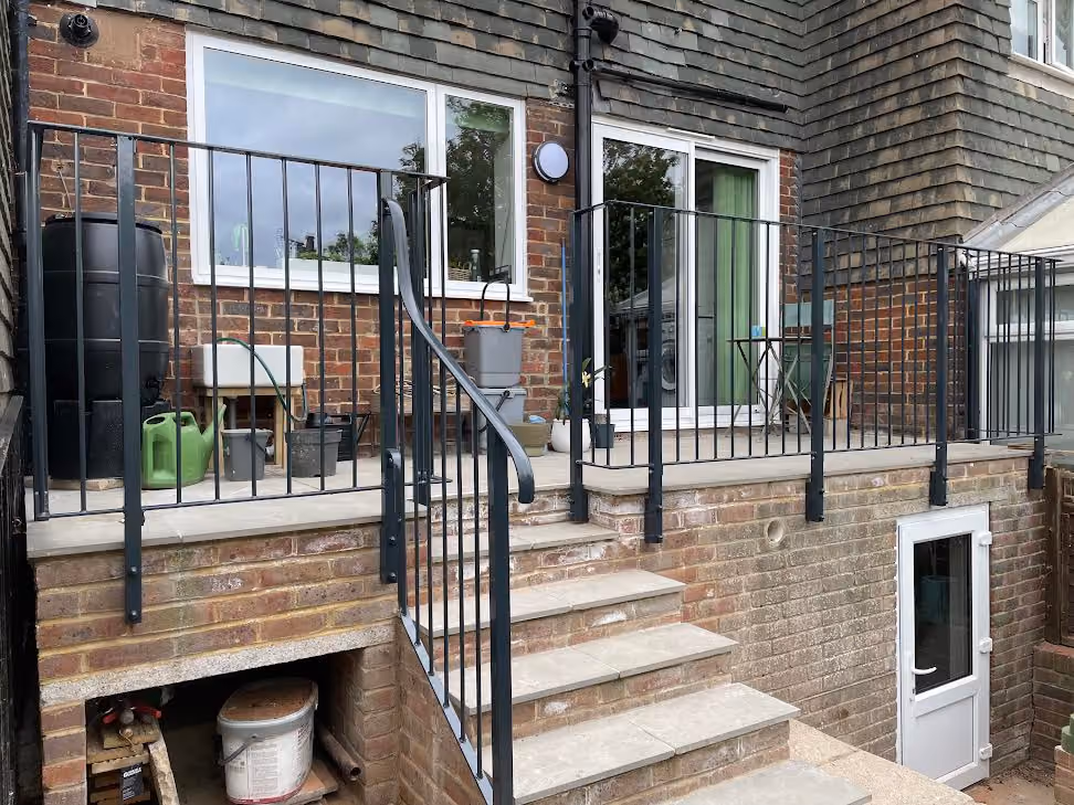 A brick house features a small balcony with metal railing and stairs leading to a lower door.