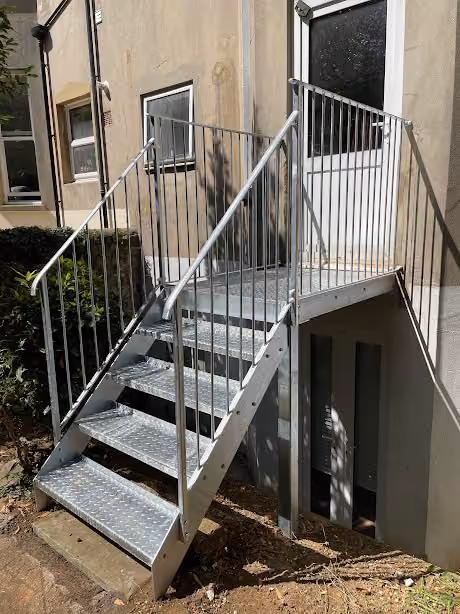Metal staircase with railings leads to a door on the side of a building.