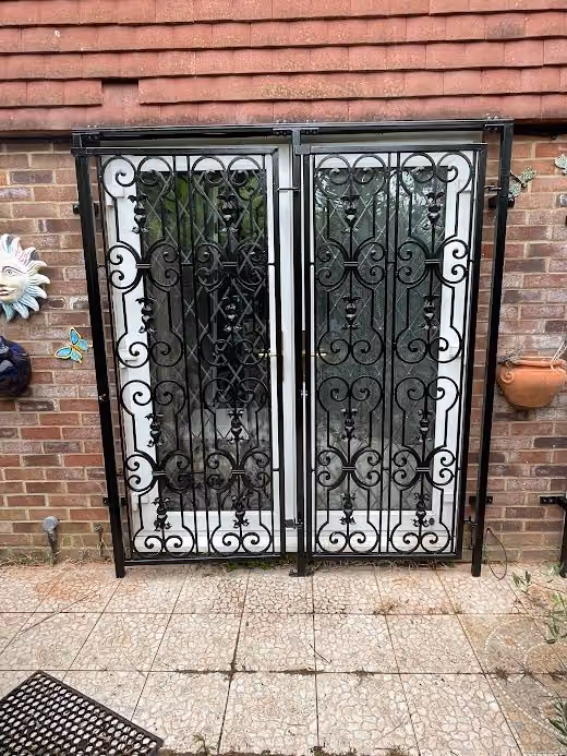 A black wrought iron gate with decorative patterns is set against a brick wall.