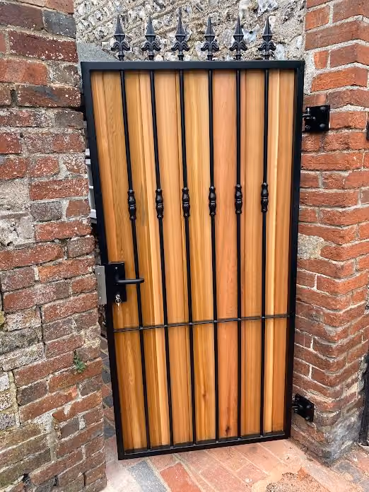 A wooden gate with a black metal frame and spiked top, set in a brick wall.