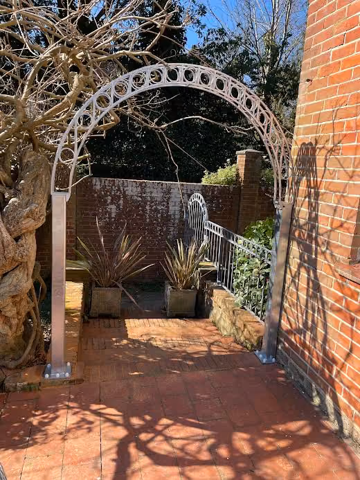 Metal archway with circular designs casting shadows on a brick path.