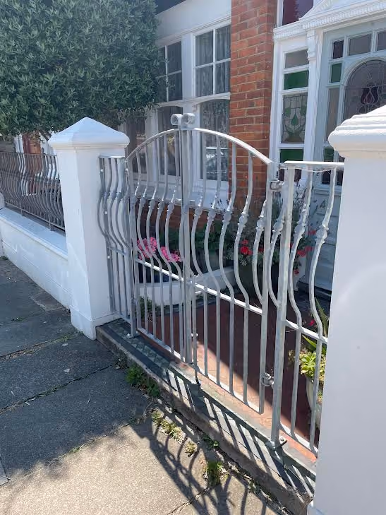 Silver metal gate with curved bars leads to a red-brick house entrance.