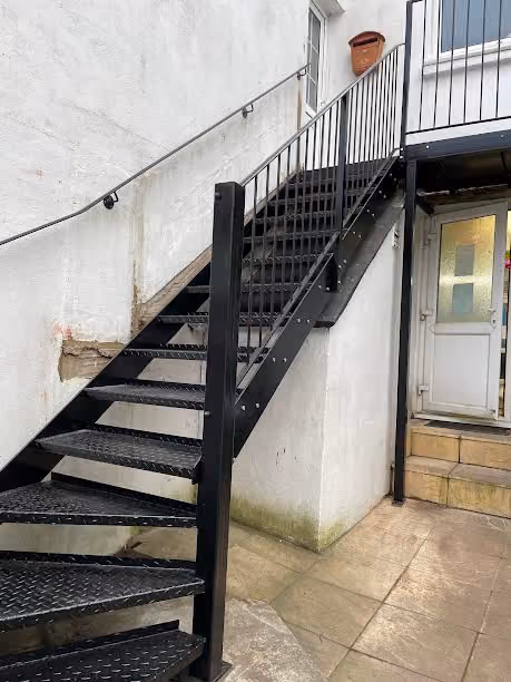 Black metal staircase leading to a door on the second floor of a white building.