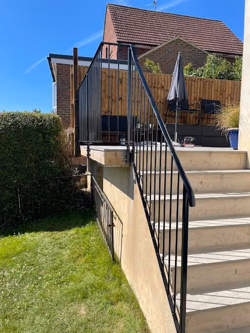 Outdoor staircase with metal railing leads to a raised patio with seating and a closed umbrella.