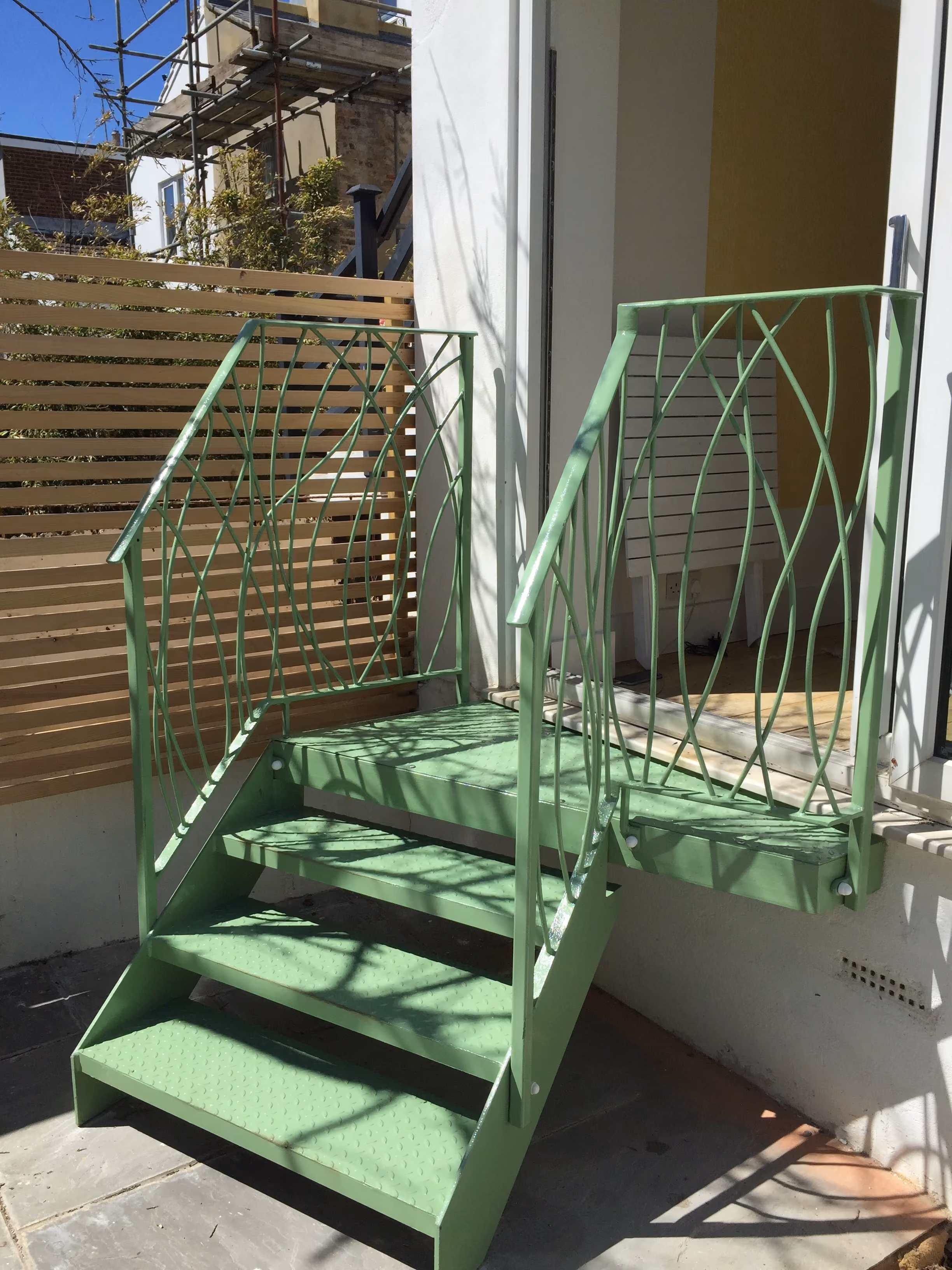 A small, green metal staircase with intricate railing leads to a doorway of a building.