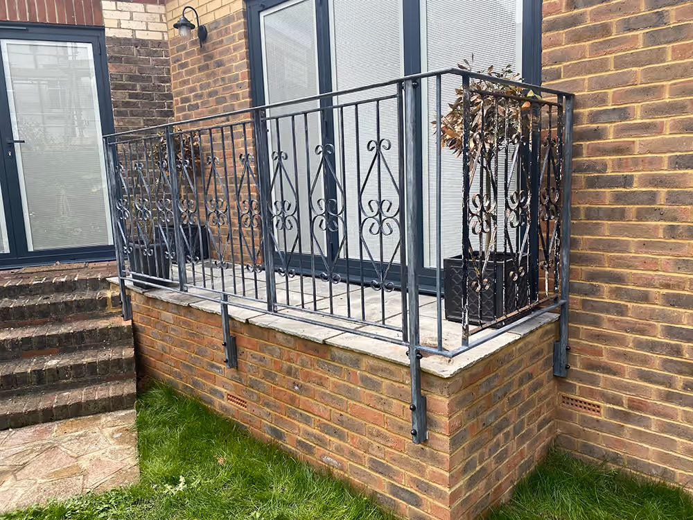 A small balcony with metal railing and potted plants on a brick house wall.