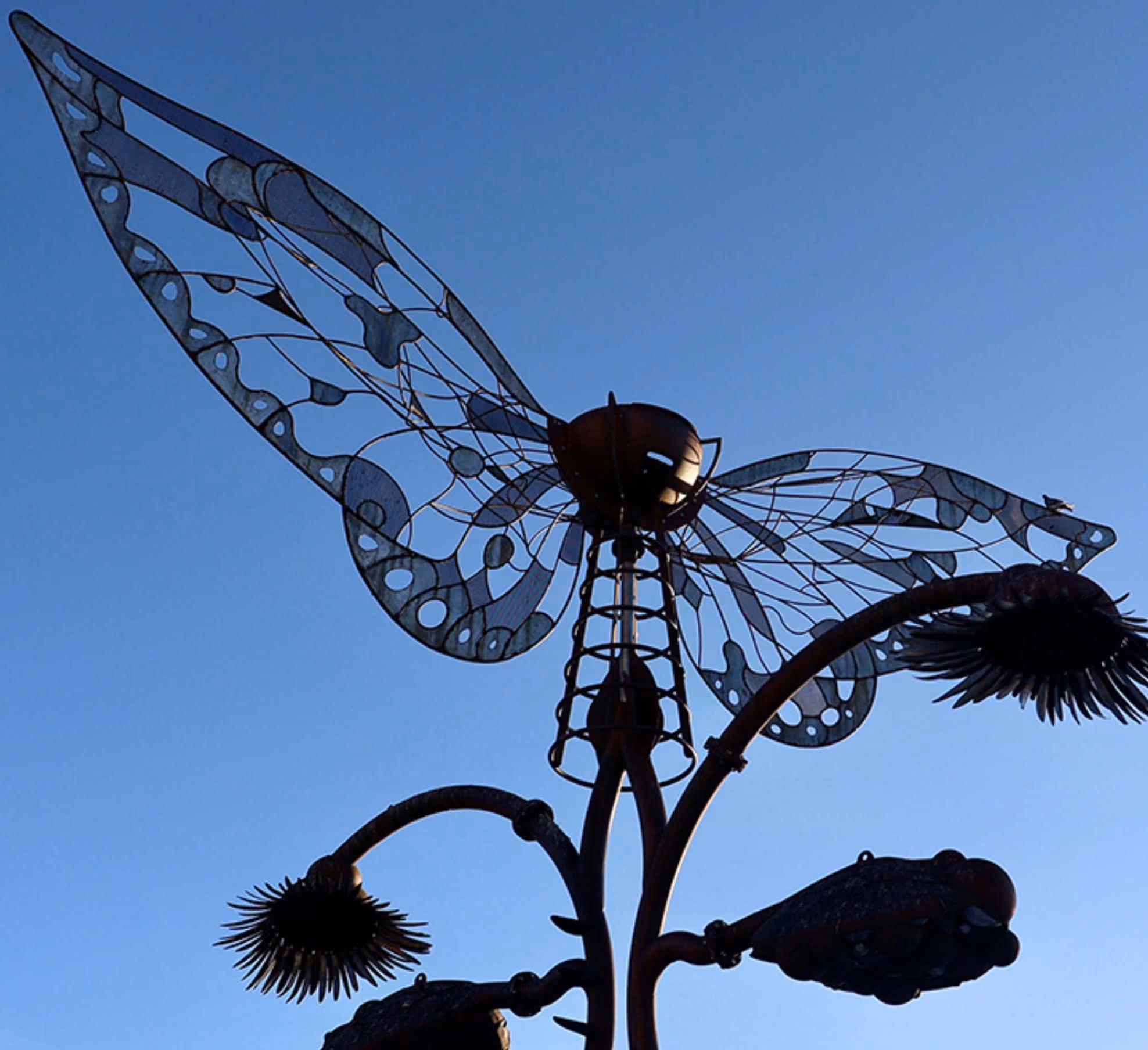 A metal sculpture of butterfly wings on a tall structure against a clear blue sky.
