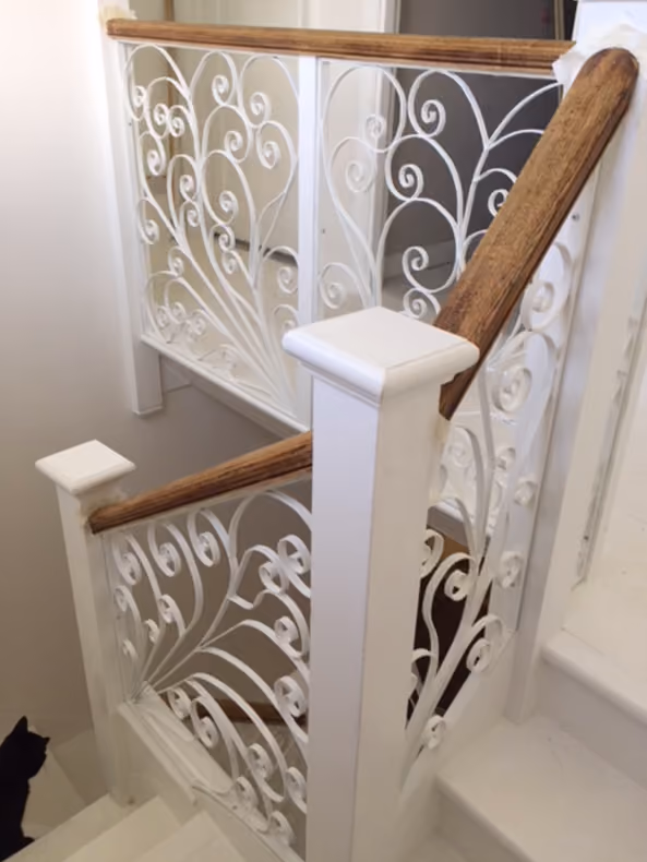 White staircase with ornate railings and wooden handrail. A black cat sits on the bottom step.