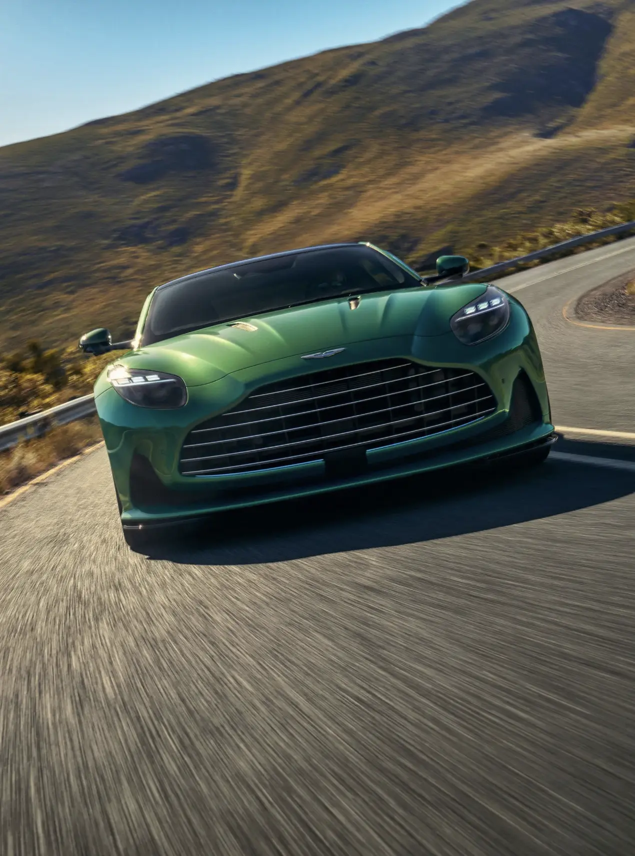 Front view of a green Aston Martin coupe driving along a mountain road.