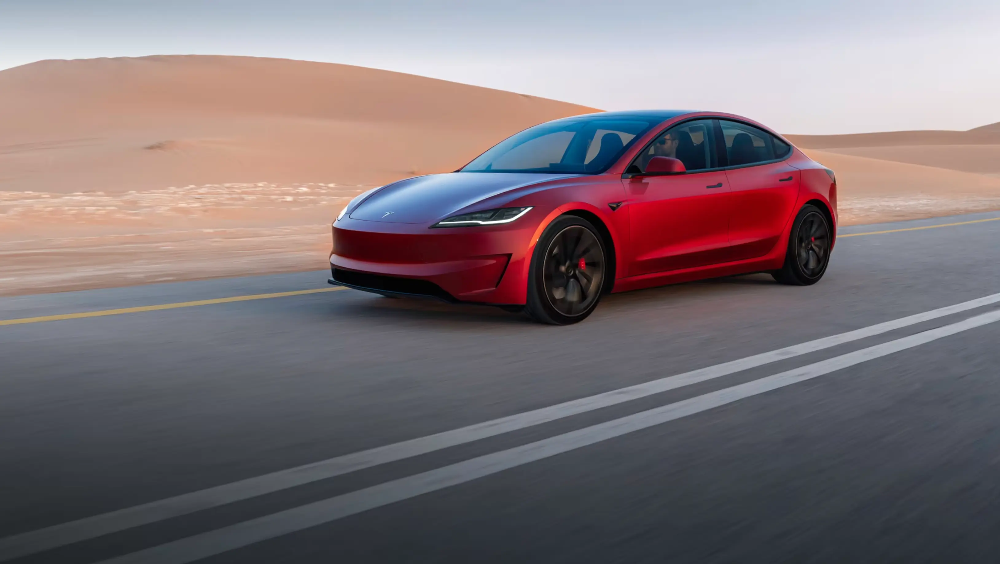 Red Tesla sedan driving along a desert road.