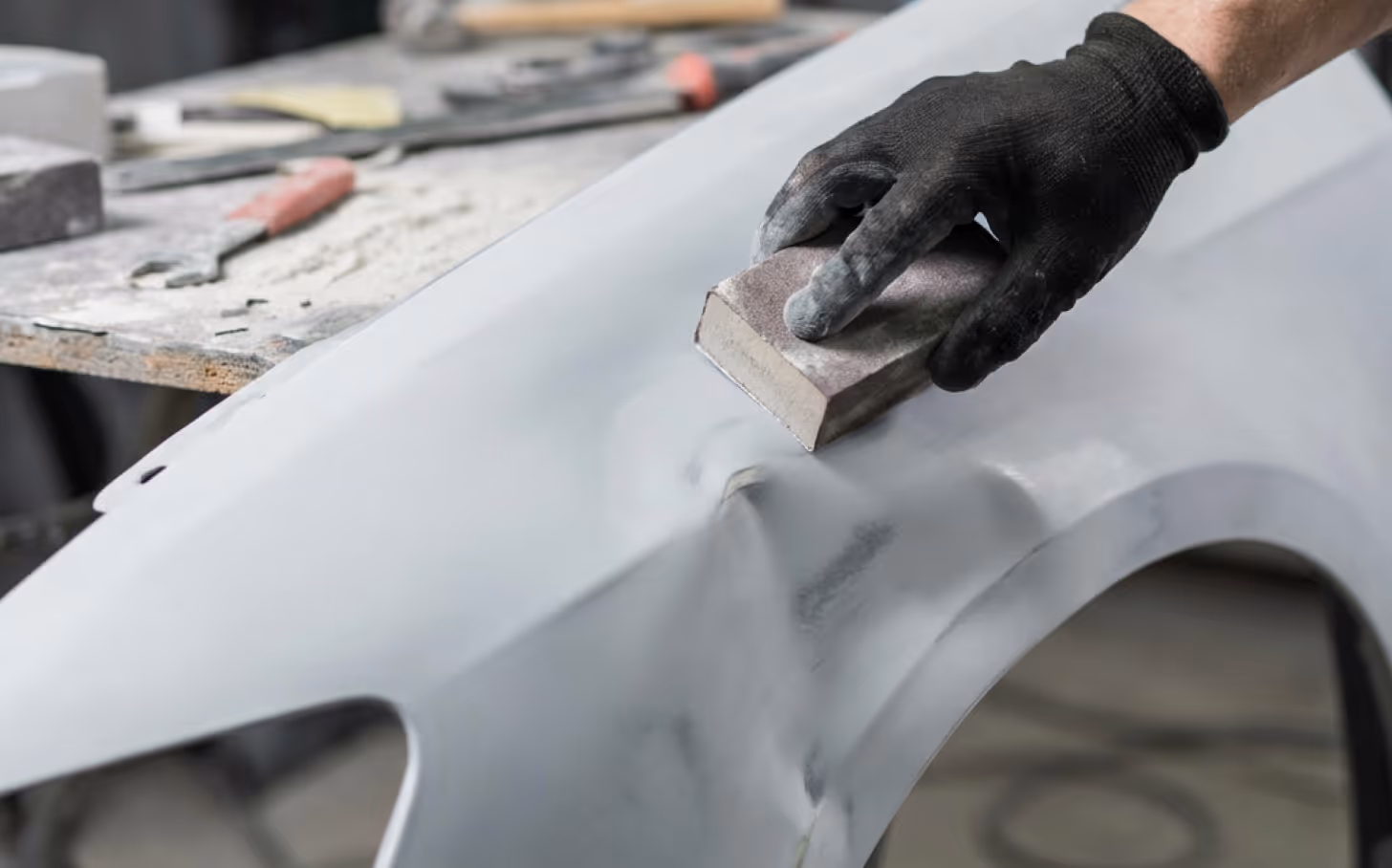 Closeup of a collision repair professional sanding the panel of a car.