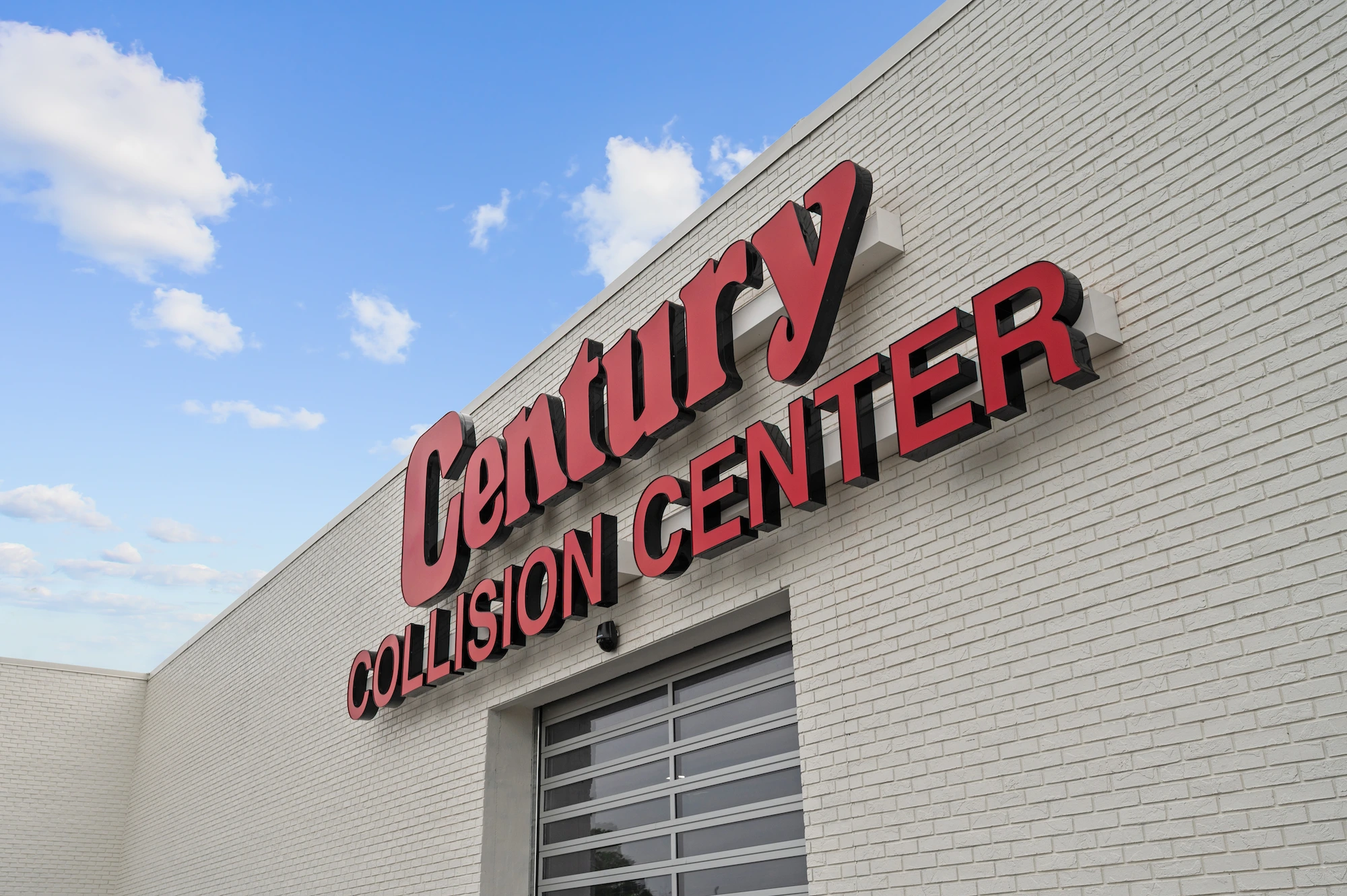 Closeup of the Century Collision Center sign on the side of a white brick building.