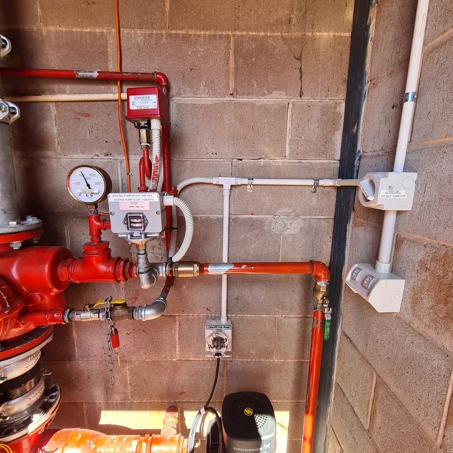 Fire-service pipework, pressure gauge and alarm equipment at a commercial site.