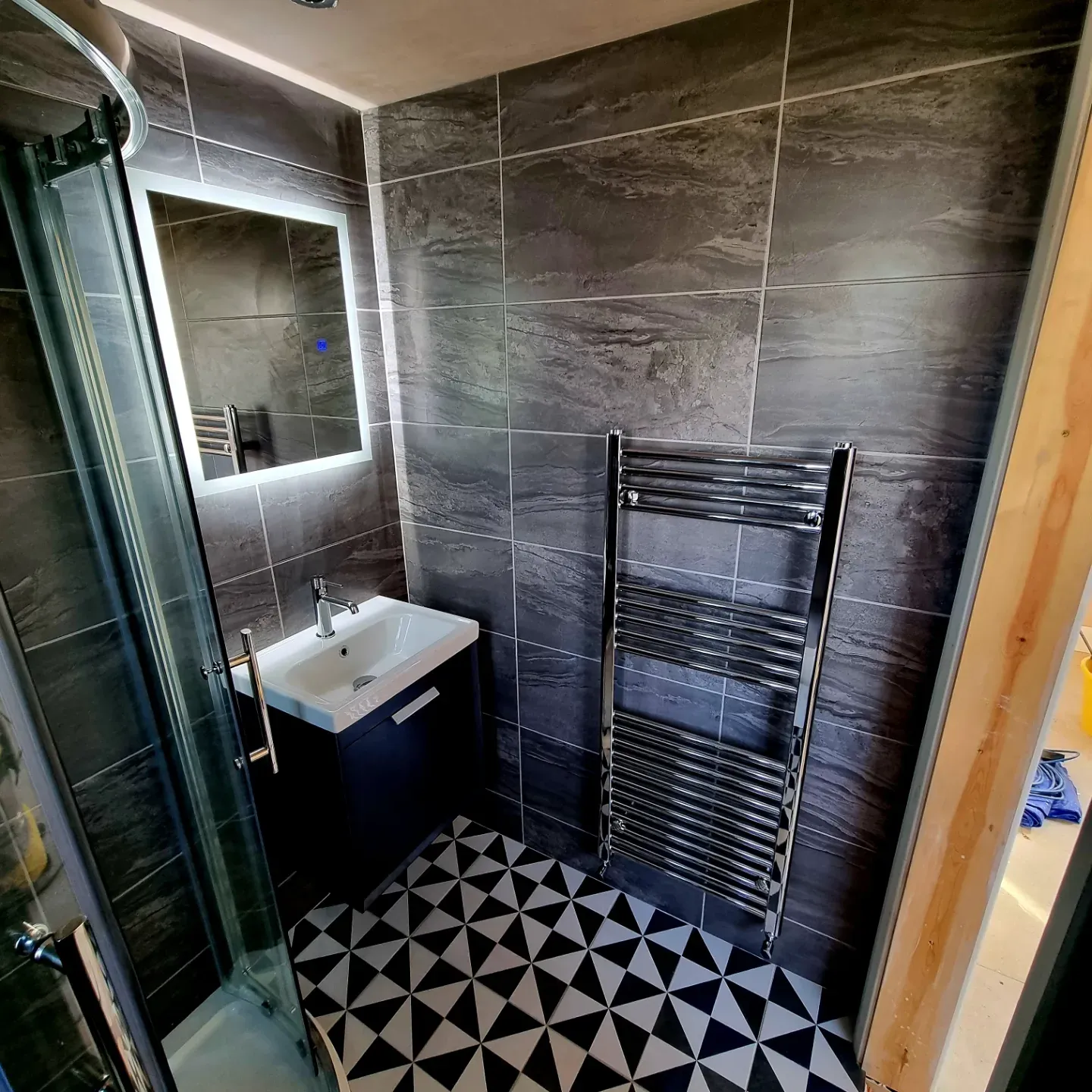 Modern bathroom with a glass shower, sink with mirror, and heated towel rail on tiled walls.