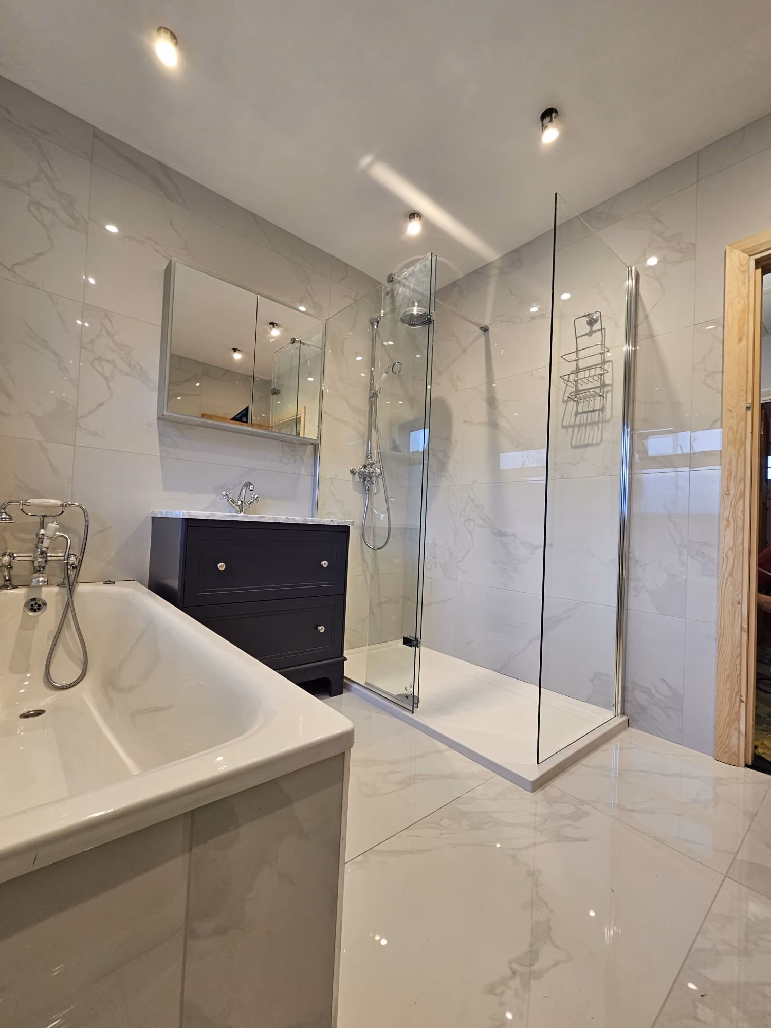 Modern bathroom with a bathtub, dark vanity, and glass-enclosed shower, featuring sleek white and gray tiles.