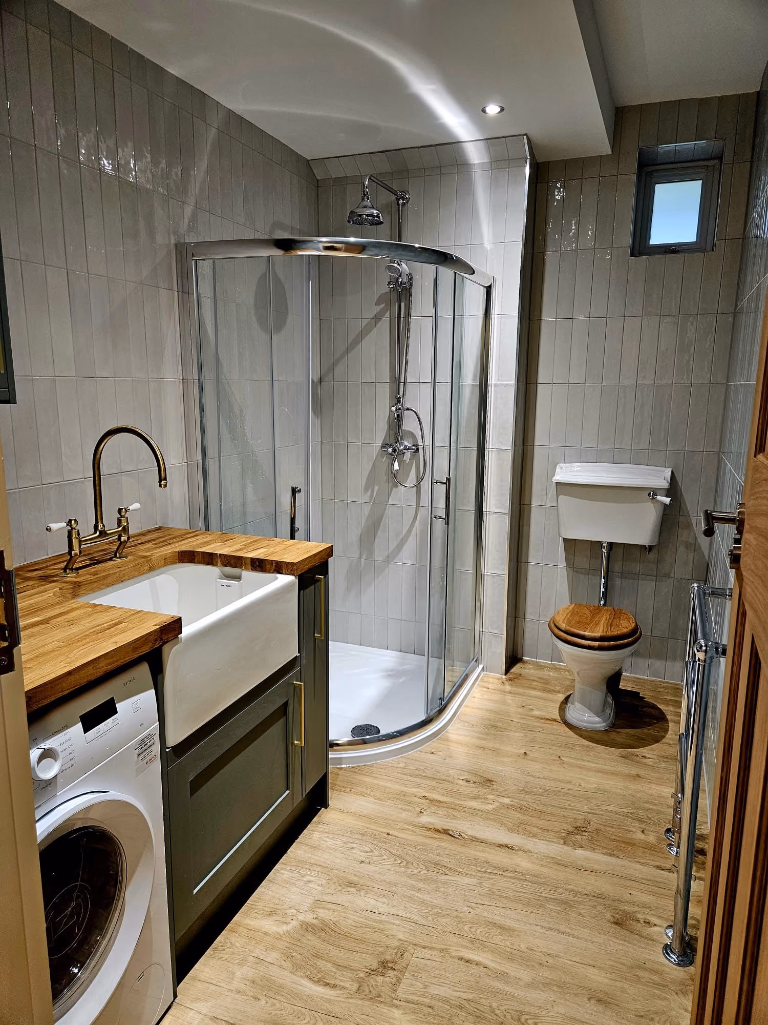 A bathroom with a shower, sink, washing machine, and toilet on a wooden floor.