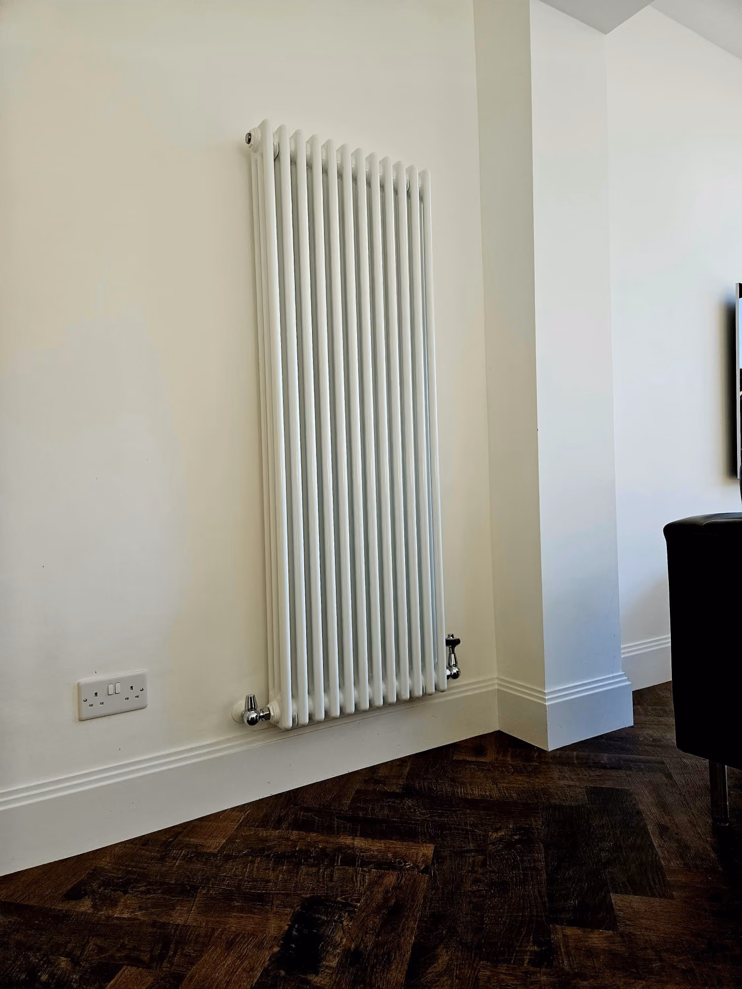 A white, vertical radiator mounted on a wall beside a power outlet.