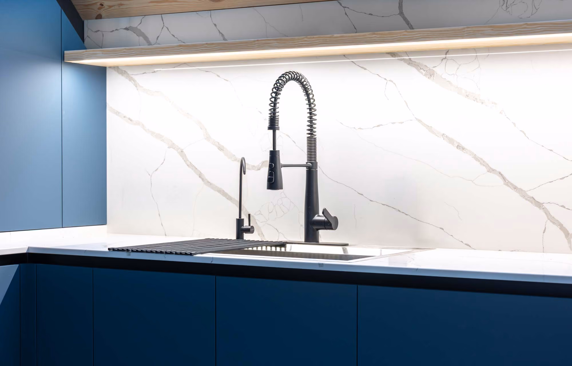 A modern kitchen sink with a tall, black faucet on a marble-patterned backsplash.