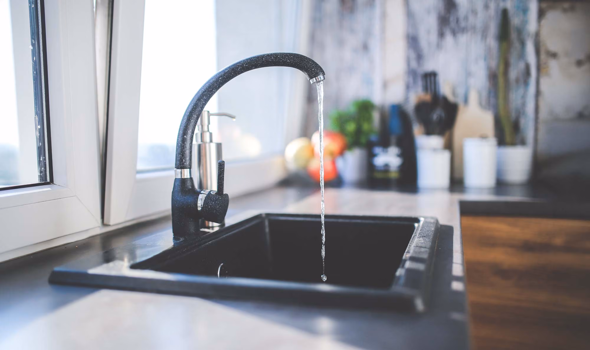 Water flows from a black kitchen faucet into a stainless steel sink.