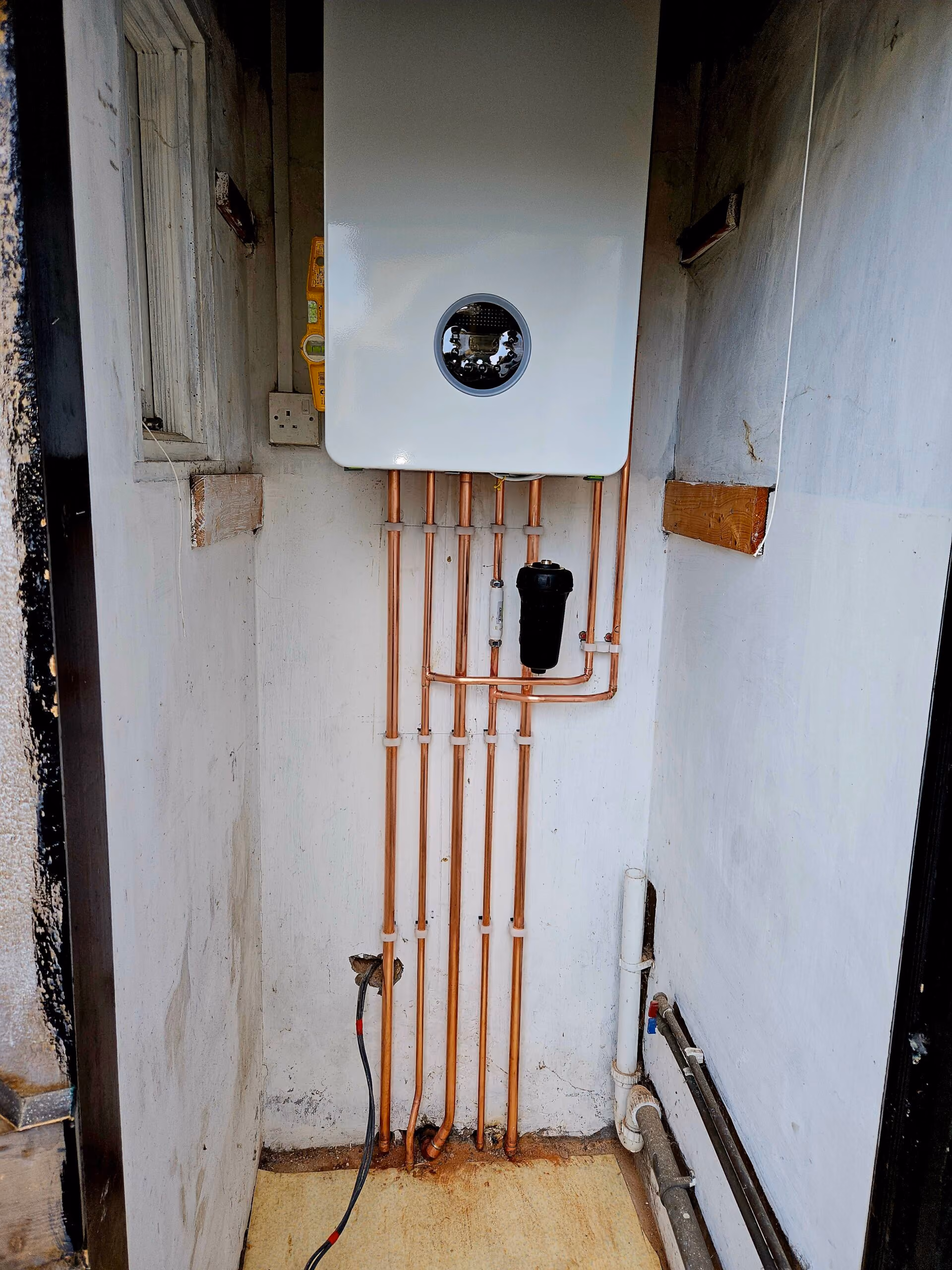 Wall-mounted boiler with connected copper pipes in a small room.