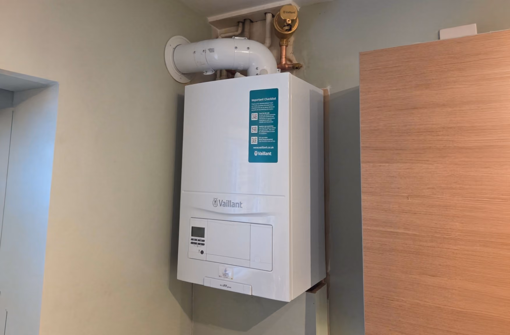 A white boiler is mounted on a wall, with visible pipes connected above.