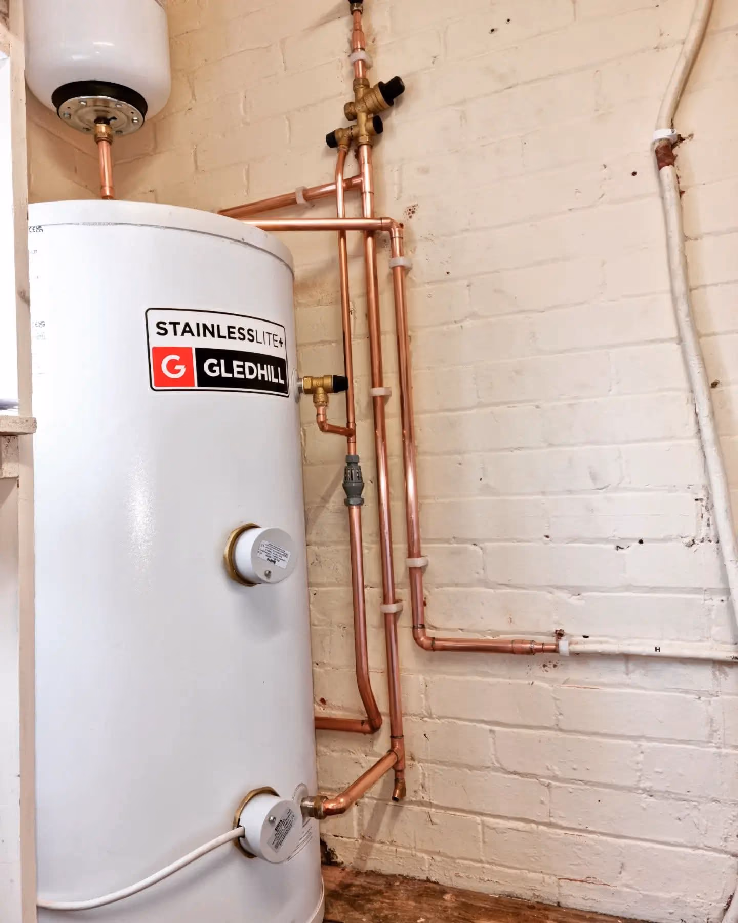 Gledhill Stainless water heater tank with copper piping against brick wall.