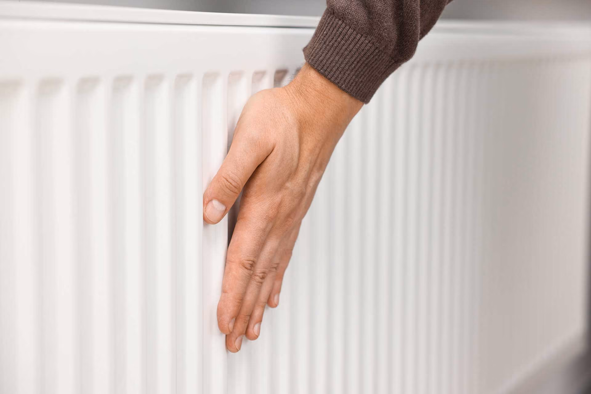 Hand touching a white radiator to test heat temperature