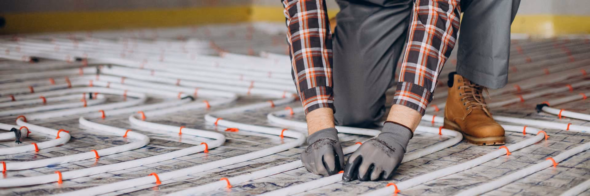 Worker installing radiant floor heating system with white tubing and red clips