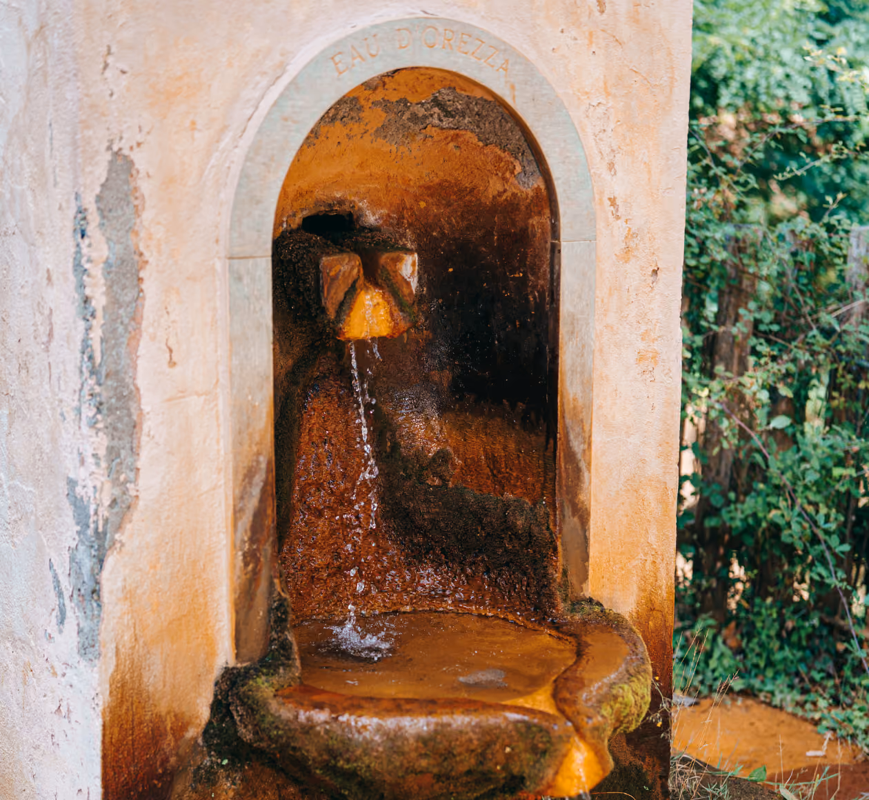 Fontaine rustique avec eau coulant d'un vieux robinet en pierre marqué Eau d'Orezza.