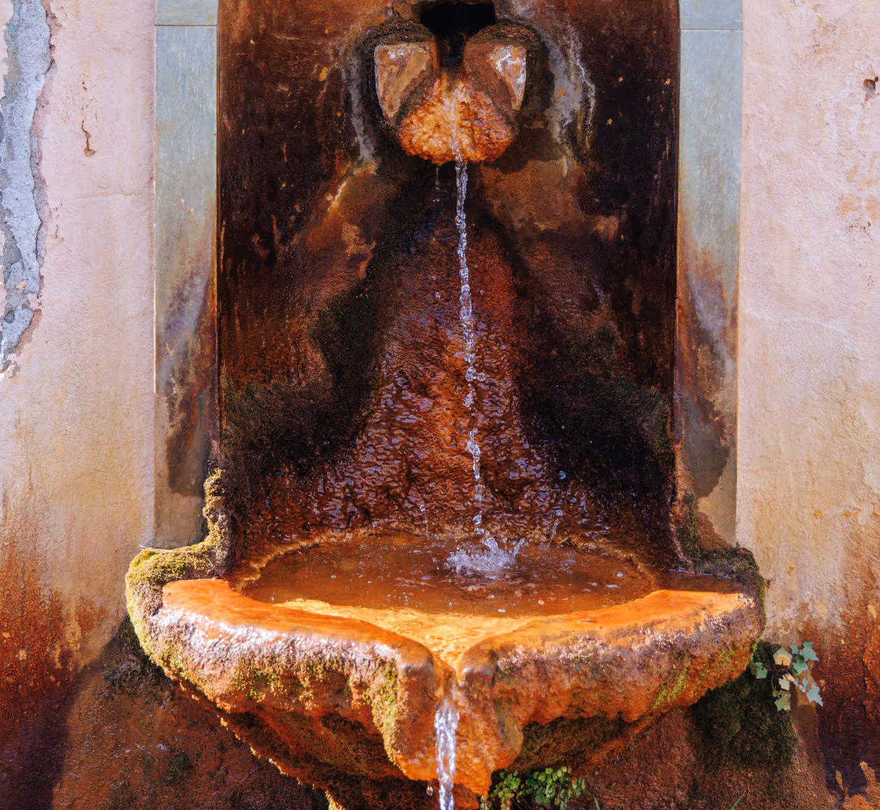 Fontaine en pierre ancienne avec de l'eau qui coule dans un bassin rouillé et mossu.