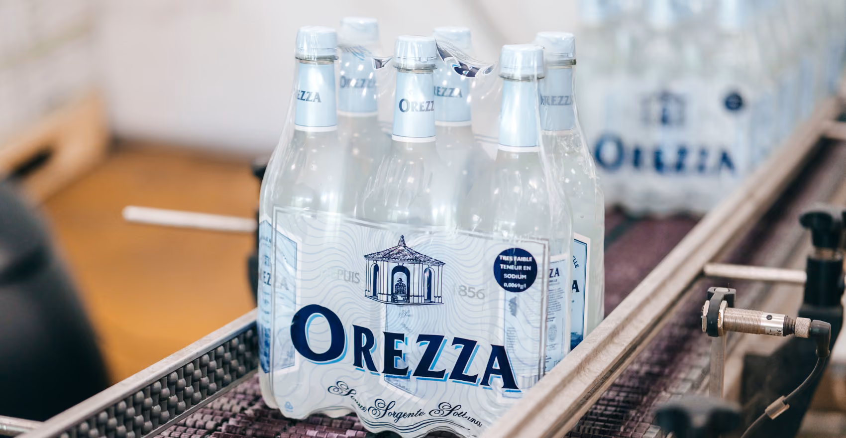 Six bouteilles d'eau Orezza conditionnées en pack transparent sur une machine d'embouteillage.