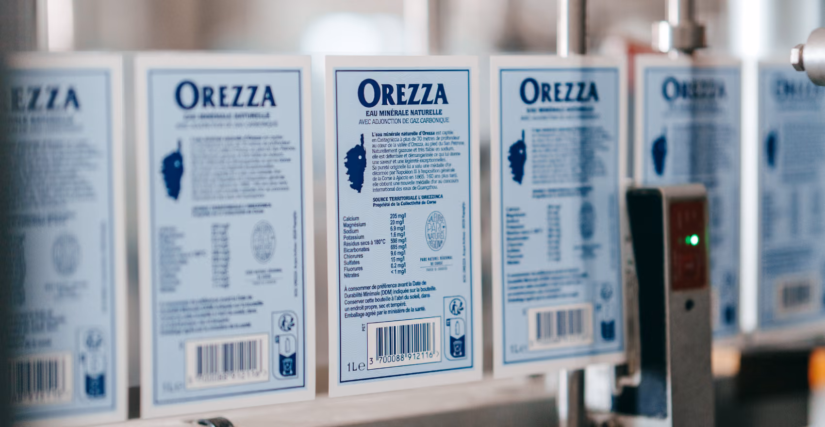 Étiquettes de bouteilles d'eau minérale Orezza alignées sur équipement d'embouteillage.