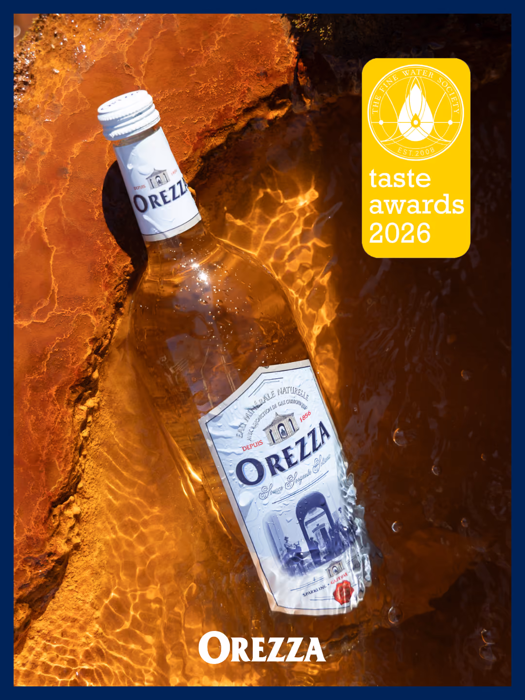 Bouteille d'eau pétillante Orezza dans l'eau sur fond ocre avec logo des Taste Awards 2026.