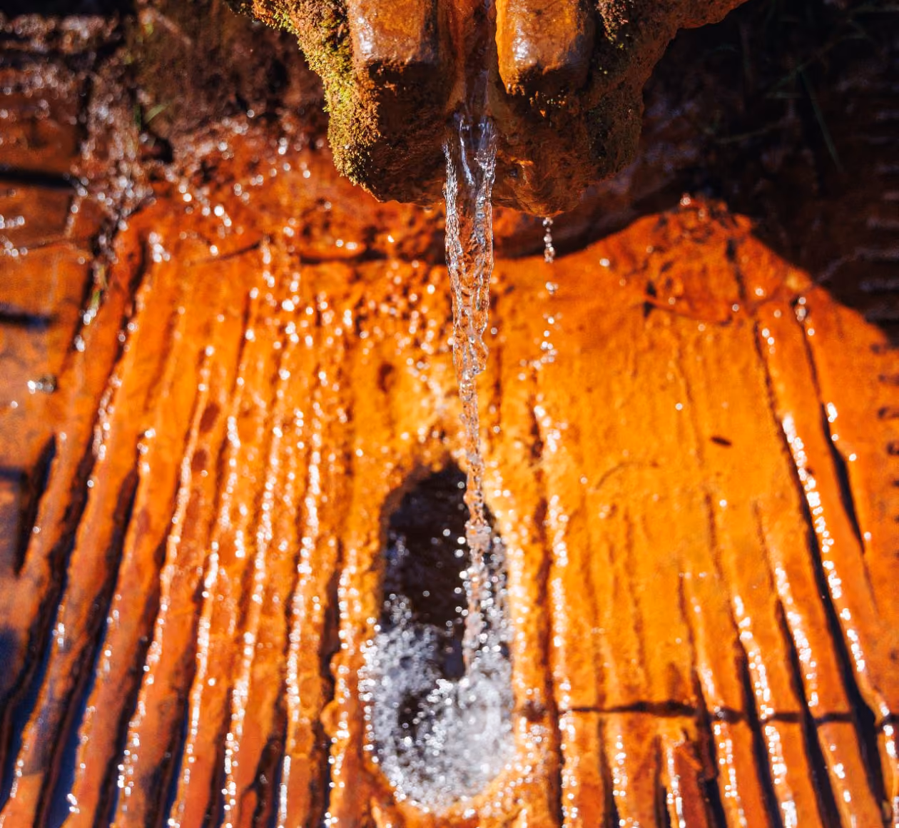 Eau claire coulant d'une source sur une roche orange avec surface texturée humide.
