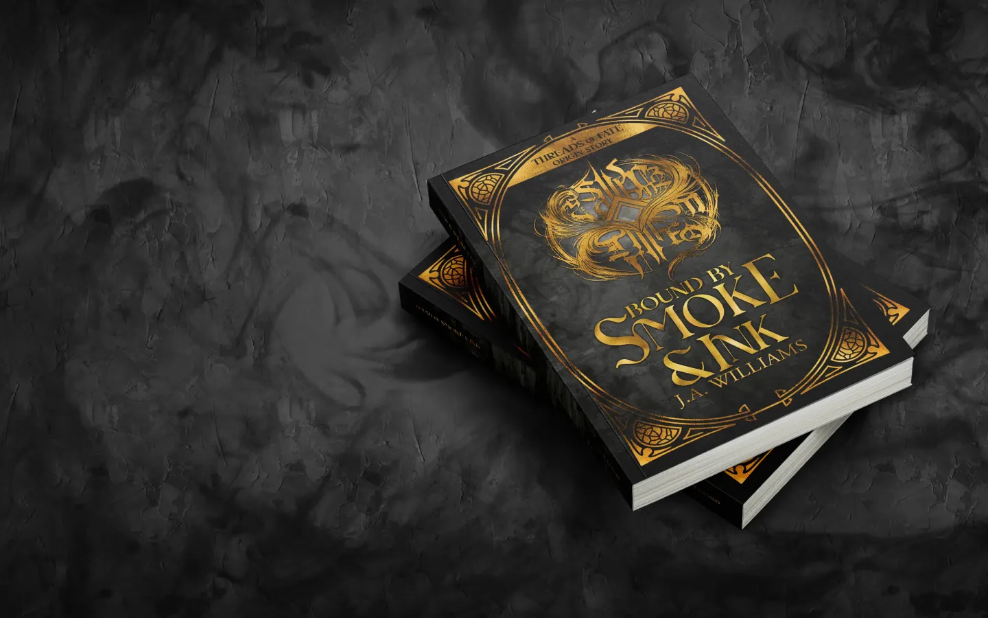 Two stacked paperback copies of Bound by Smoke & Ink by J.A. Williams, the black and gold prequel novella to the Threads of Fate series