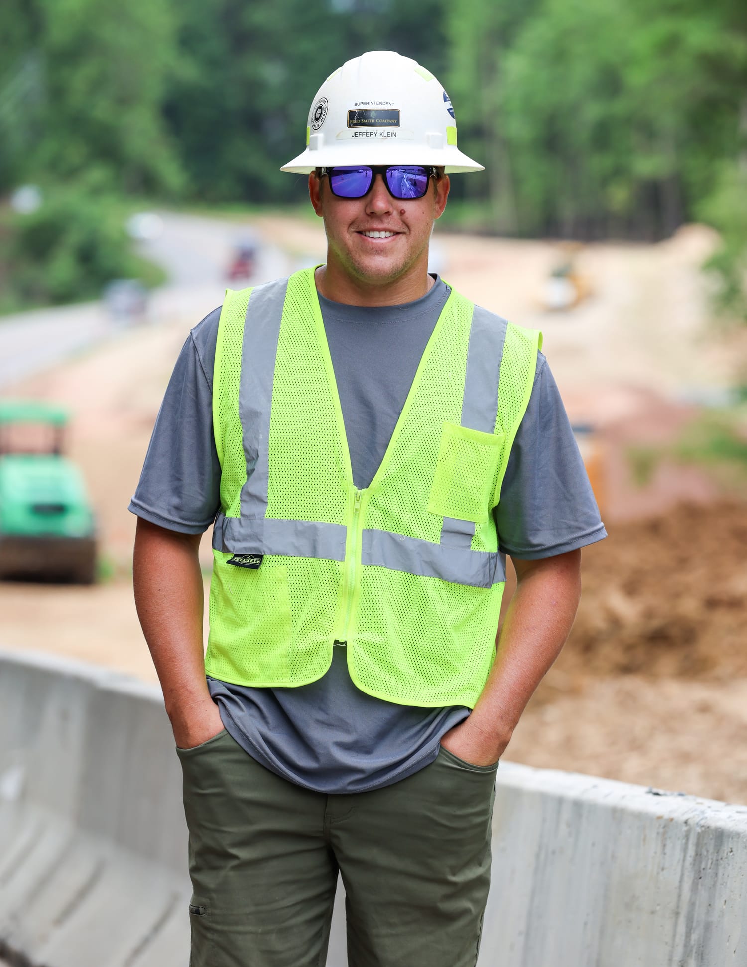 Smiling crew member in a hard hat and safety vest on a road project