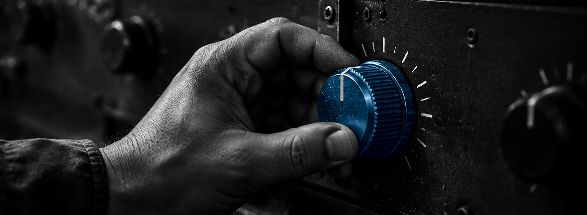 A hand turns a blue control knob on a dark equipment panel.