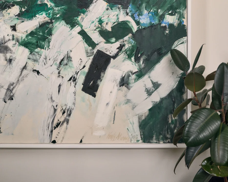 Minimalist hallway with abstract red and green painting and a console table with lamp and plant.