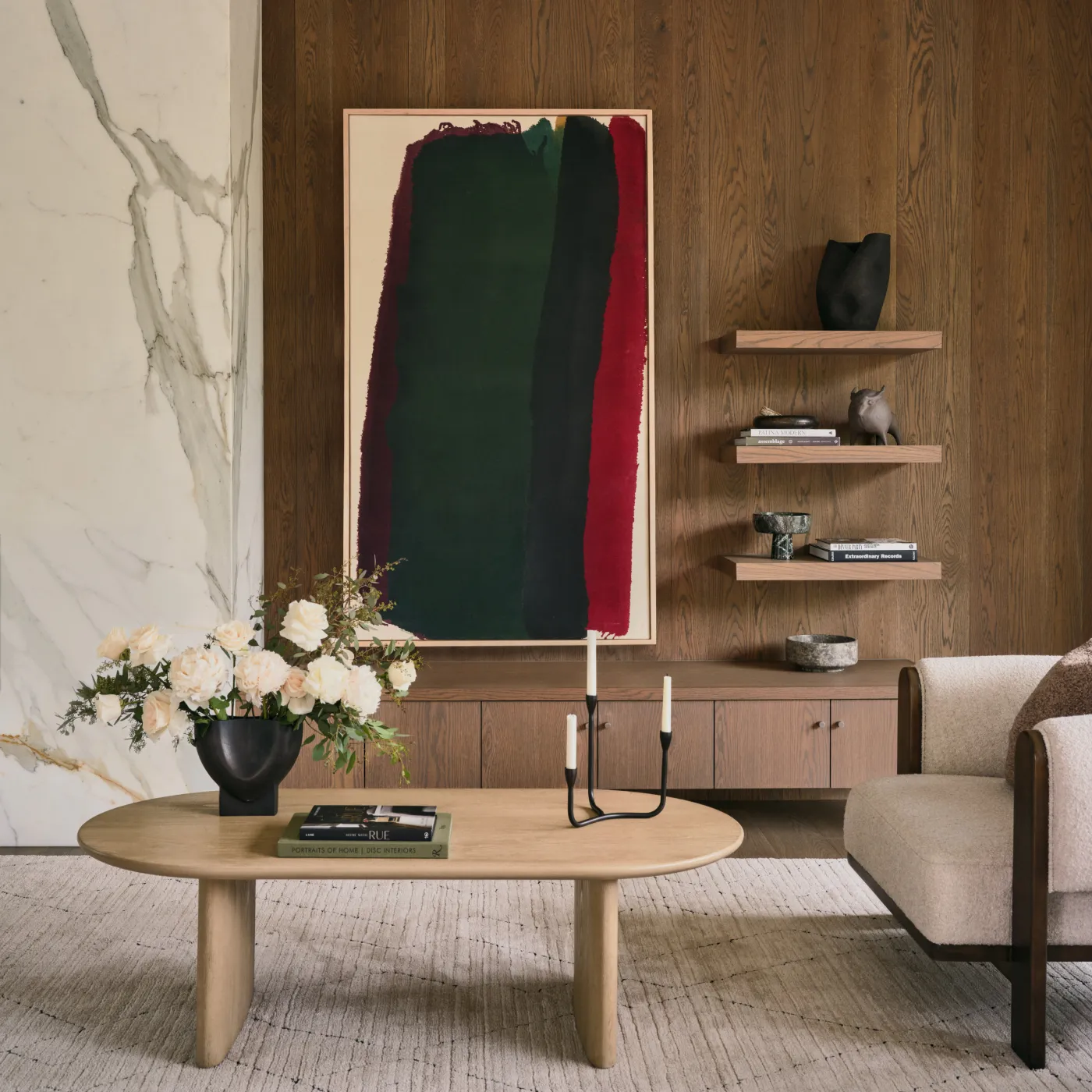 Modern living room with wooden walls, abstract painting, beige sofa, oval coffee table, flowers, and candles.