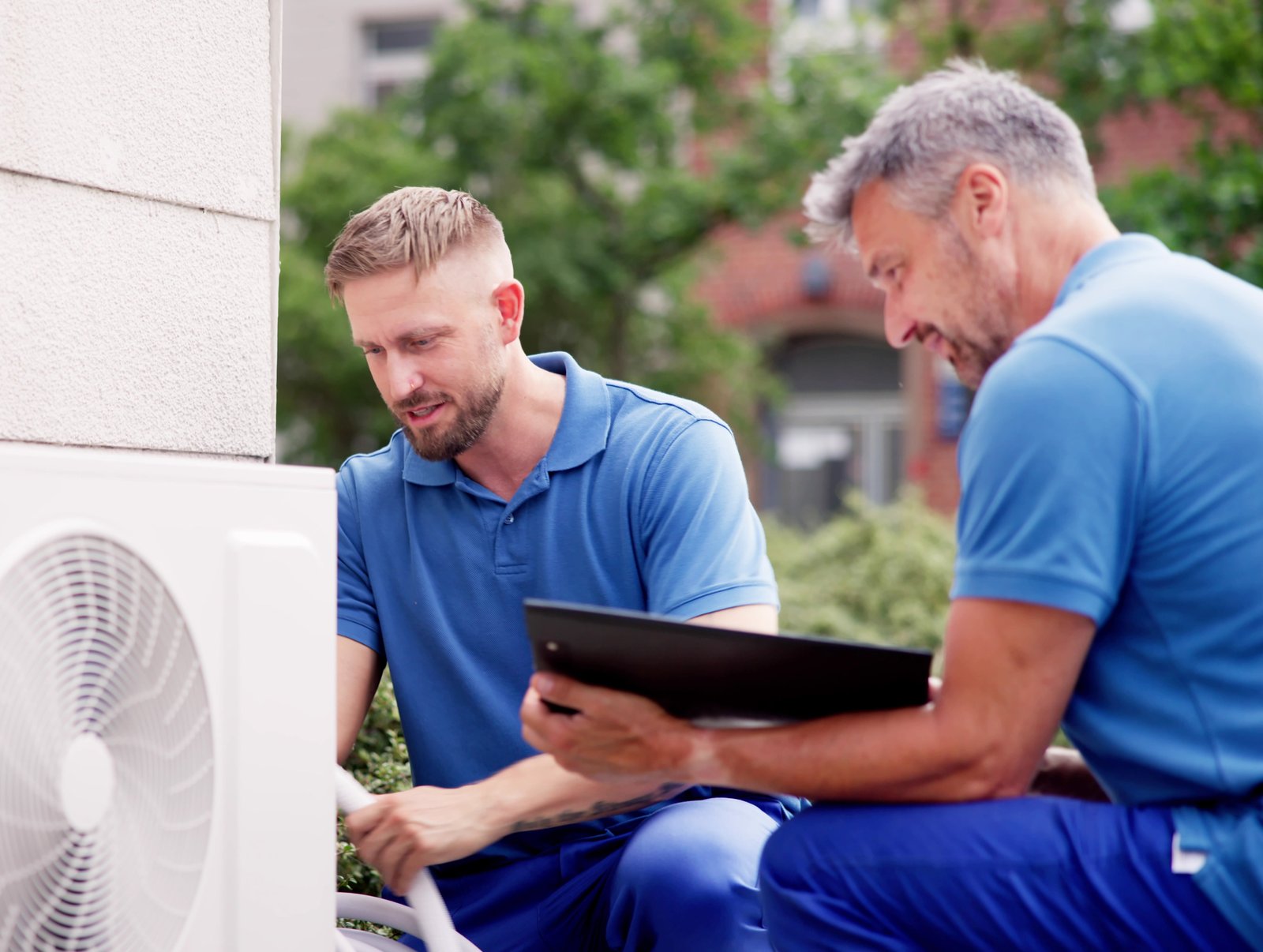 Two HVAC technicians servicing an outdoor air conditioning unit