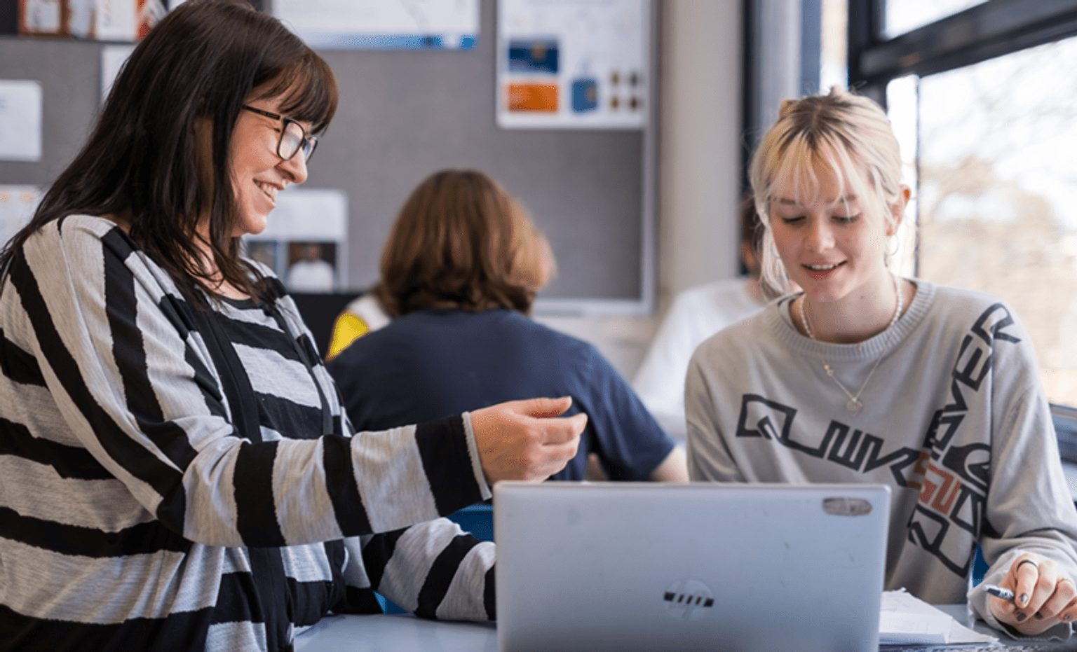 Three teachers collaborating around a laptop in a school workspace