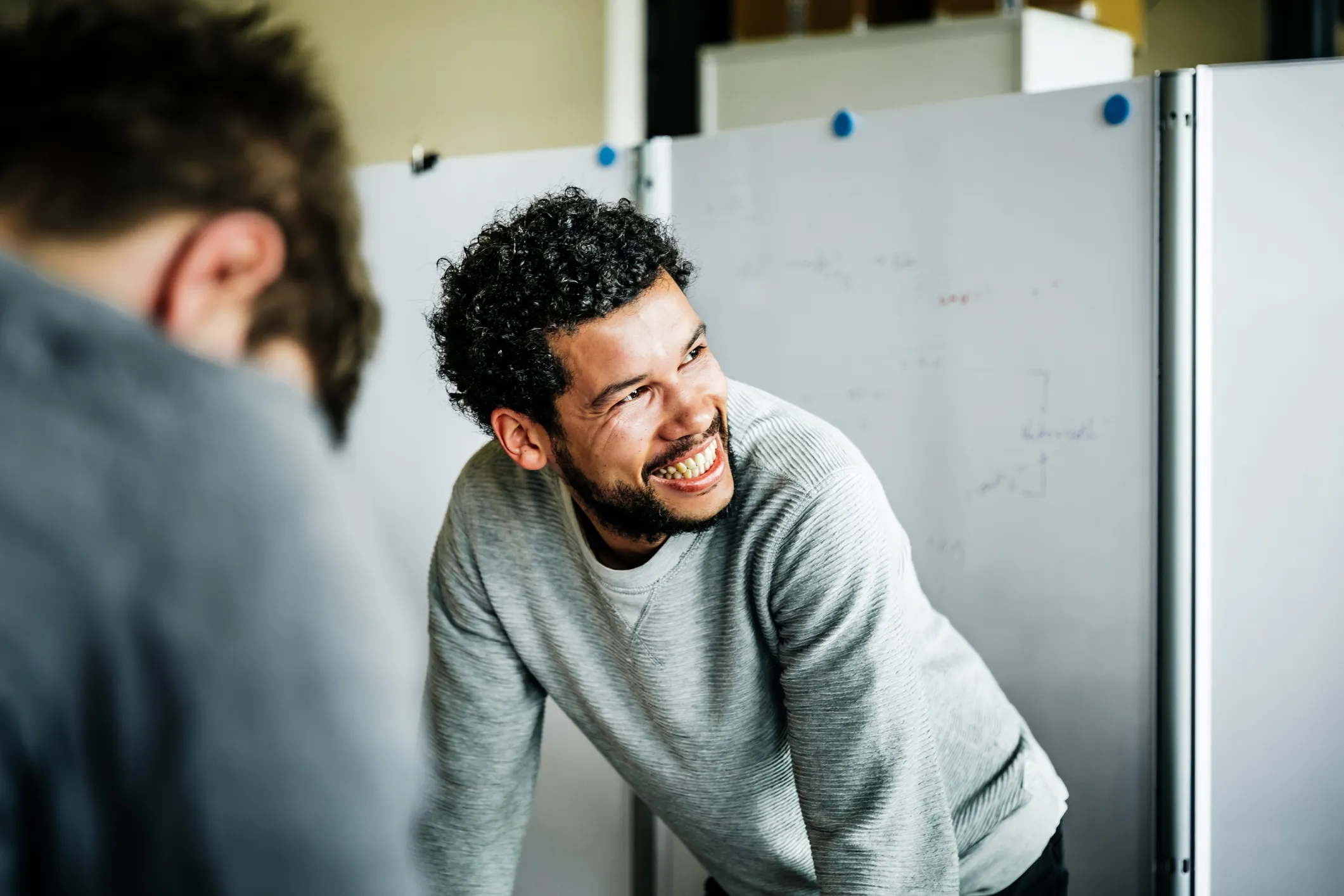 A man leaning on a whiteboard, laughing, during a workshop