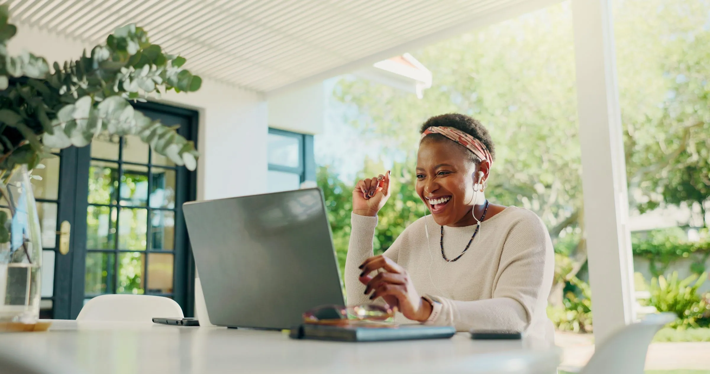 A woman working at a laptop in a bright room looking out to a garden