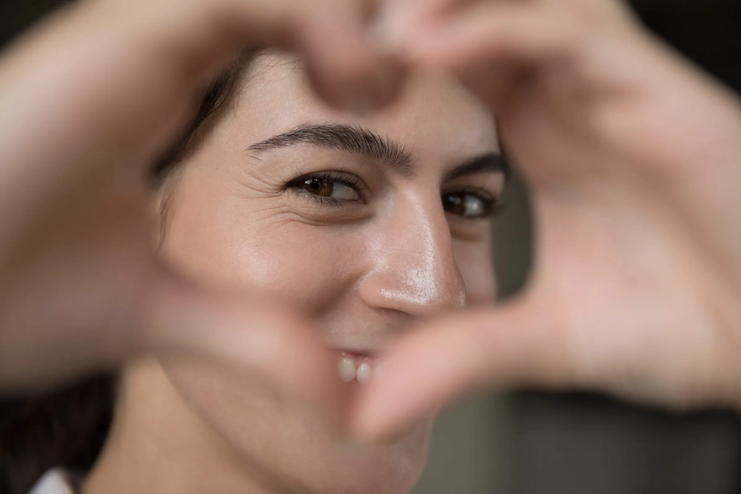 A woman smiling, making a heart shape with her hands in front of her face